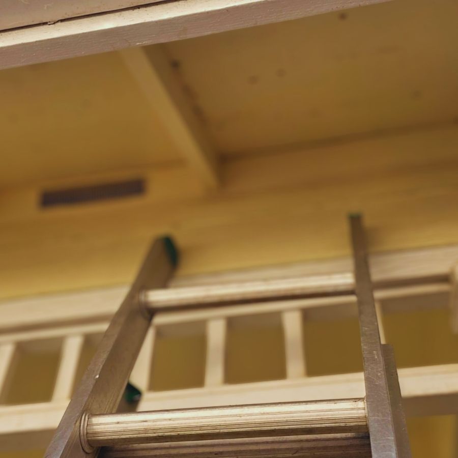 image shows ladder leaning on house for roof damage inspection under the eaves