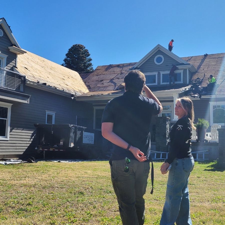 view of a man and woman talking and assessing a roof condition amid tear-off